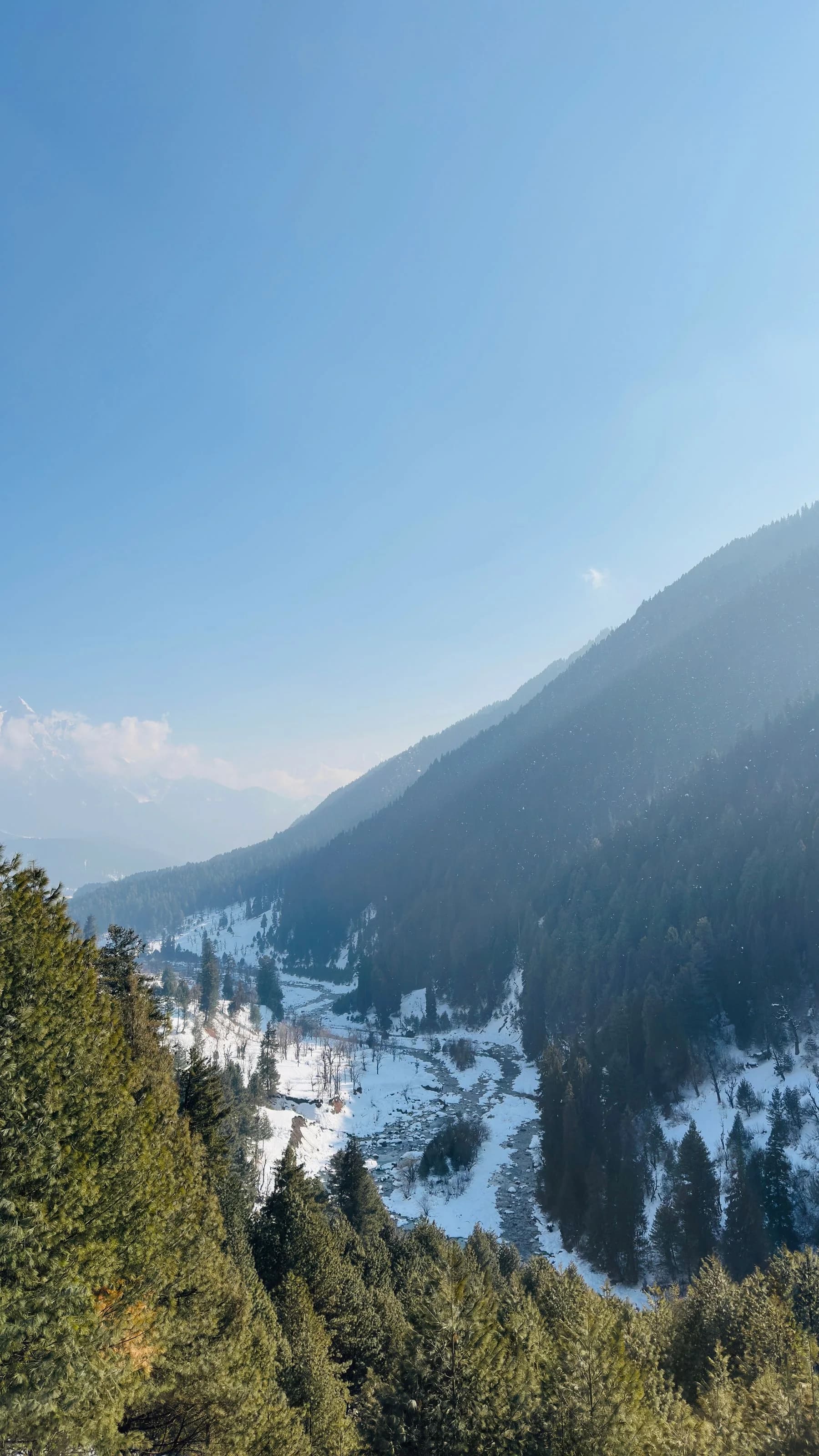Snow along the river and forested mountains in Pahalgam during winter
